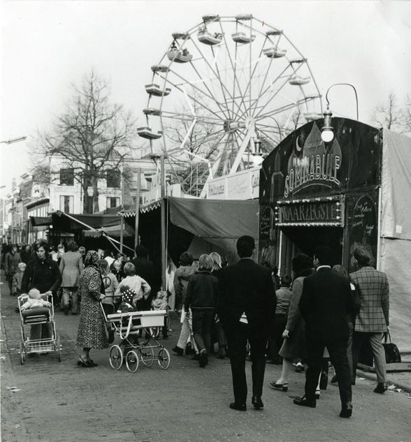 Gorinchem: Kermis op de Kalkhaven, waarschijnlijk november 1963. Toen werd Gorinchem verrast door de 'para-trooper', een hoog, scheefdraaiend rad met gondels. Op de voorgrond zien we Madame Somnabule de waarzegster. In haar glazen bol ziet ze geluk en voorspoed, tenminste dat hoop je. Naast de waarzegster staat een echte Hollandse gebakskraam. Volwassenen maar ook kinderen in wandelwagens keken hun ogen uit. Het gerinkel van blikjes die worden omgegooid, maakt een diepe indruk.