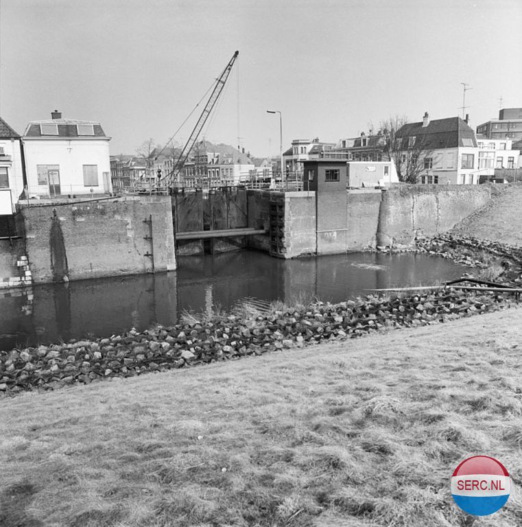 Gorinchem: De Kleine Merwedesluis in 1986 met een tijdelijke afdamming die het werken aan de sluis mogelijk maakte. De Kleine Merwedesluis was een schutsluis tussen de Lingehaven van Gorinchem en de Merwede. De sluis is vervangen door de Lingesluis op dezelfde plaats. De bijbehorende voormalige brugwachterswoning werd gebouwd in 1910 naar een neorenaissance-ontwerp van A.A.H.W. König. De woning bevat een gevelsteen uit 1640. De sluis werd ook wel Oude Merwedesluis genoemd, dit ter onderscheiding van de veel later gebouwde Grote Merwedesluis tussen het Merwedekanaal en de Merwede die ook wel als Nieuwe Merwedesluis bekend staat .