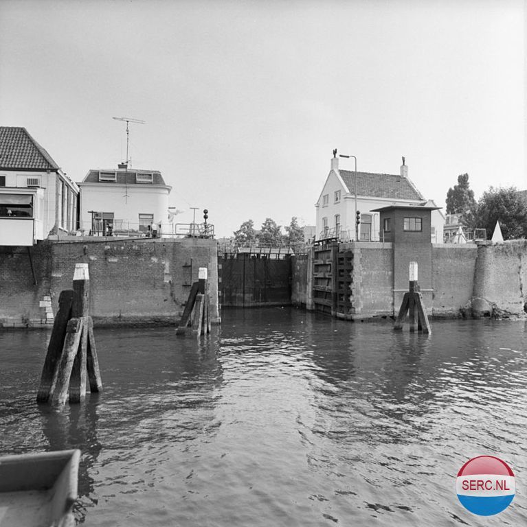 Gorinchem: De Kleine Merwedesluis in 1982 gezien vanaf de rivierkant. De Kleine Merwedesluis was een schutsluis tussen de Lingehaven van Gorinchem en de Merwede. De sluis is vervangen door de Lingesluis op dezelfde plaats. De bijbehorende voormalige brugwachterswoning werd gebouwd in 1910 naar een neorenaissance-ontwerp van A.A.H.W. König. De woning bevat een gevelsteen uit 1640. De sluis werd ook wel Oude Merwedesluis genoemd, dit ter onderscheiding van de veel later gebouwde Grote Merwedesluis tussen het Merwedekanaal en de Merwede die ook wel als Nieuwe Merwedesluis bekend staat .