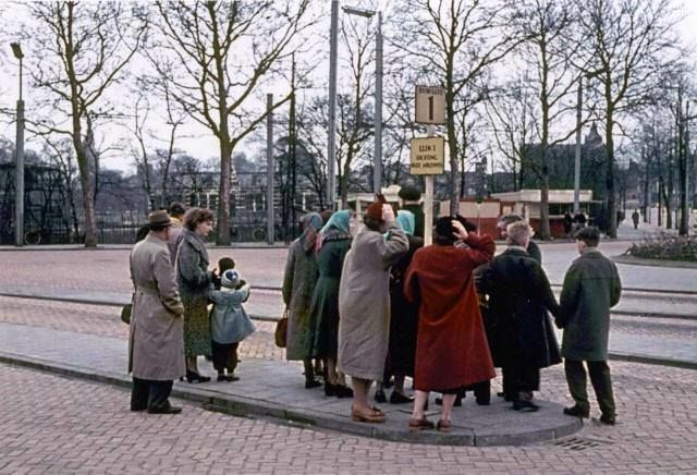 Nijmegen 1956: Stationsplein. Wachten bij de bushalte op Lijn 1, de Stadslijn, van de Centrale Vervoersdienst. | Geheel rechts nog de oude Spoorstraat met op de achtergrond het Kolpinghuis. Achter het terrein van de Gemeentelijke Gasfabriek. In het midden is tussen de bomen de St. Josephschool aan de Nieuwe Marktstraat zichtbaar.