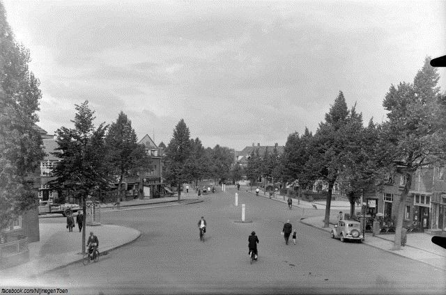 Nijmegen 1957: Daalseweg, Altrade. | Altrade ligt in het stadsdeel Nijmegen-Oost. We kijken naar het kruispunt, van links naar rechts, Koolemans Beynenstraat - Daalseweg - Heydenrijckstraat - Van Langenveldstraat - Tooropstraat. Een rustige buurt zo te zien, mede door het weinige verkeer in die tijd. Een vader met zijn kind aan de hand loopt midden op straat. Let ook eens op de telefooncel links op de foto. In Altrade is van oudsher altijd relatief veel middenstand en horeca gevestigd geweest.