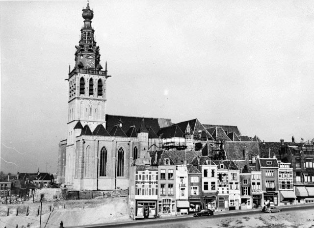 Nijmegen 1953: Deze foto is genomen vanaf de Houtstraat. We zien de bijna geheel gerestaureerde St. Stevenskerk die in 1944 met het bombardement zwaar beschadigd raakte. Een deel van de bebouwing aan de Stikke Hezelstraat kwam redelijk ongeschonden uit het oorlogsgeweld zoals goed te zien is op deze foto.