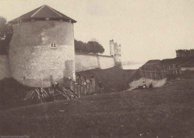 Nijmegen 1875: Deze foto uit 1875 van fotograaf Gerard Korfmacher toont de stadsmuur van Nijmegen in de richting van de Waal. We staan precies op de plek van het huidige Hunnerpark. Op de voorgrond is de St. Joosttoren te zien en op de achtergrond de Belvédère. De zware ronde St. Joost-(of Joris)toren was een restant van een middeleeuwse stadspoort, de St. Joost- of Ubbergsepoort uit 1436 en lag ter hoogte van de huidige St. Jorisstraat. De poort werd al voor 1500 dichtgemetseld. Voor de poort hield de Nijmeegse Schutterij vroeger schietoefeningen in de droge gracht. Het Hunnerpark is aangelegd na de afbraak van de stadsmuren tussen 1876 en 1882. Helaas is de St. Joosttoren bij de afbraak van de stadsmuren ook gesloopt.