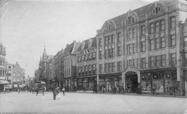 Nijmegen 1925: We nemen u terug naar de Grote Markt omstreeks 1925. Vanaf de Kerkboog kijken we in de richting van de Korte Burchtstraat. Rechts zien we het statige pand van Vroom & Dreesmann, daarnaast de Kledingzaak van Van Dijk & Witte. Links daarvan de torenspits van het pand van Bahlmann. Uiteraard mag de tram niet ontbreken op dit mooie stukje Nijmegen.