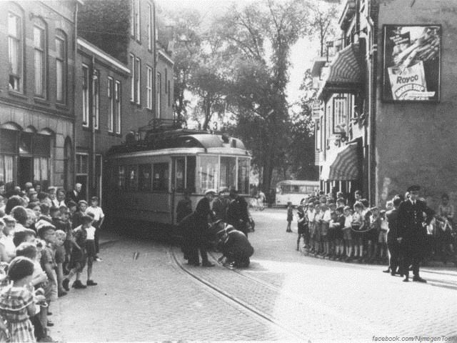 Nijmegen: Op 6 juni 1955 ontspoorde tramlijn 3 door een wielbreuk op de Doddendaal. Een groot vermaak voor met name de Nijmeegse jeugd, die er in grote getalen op afkwam om dit schouwspel niet te missen. Terwijl men bezig is om de schade aan de rails te bekijken houdt een agent het publiek op een afstand en het verkeer tegen. Rechtsbovenin zien we een reclamebord van 'Royco Groentensoep, van de beste groenten'.