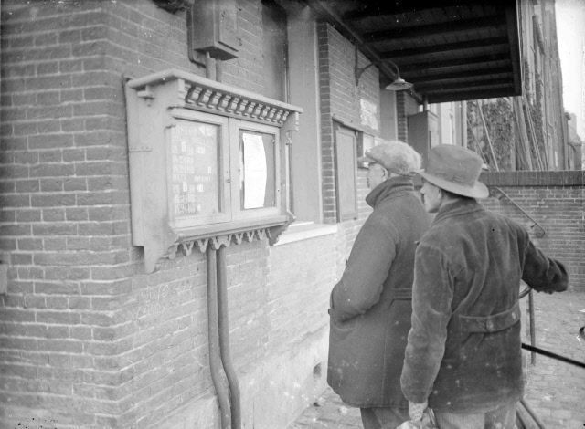 Nijmegen: De Waalkade in 1933. Het mededelingenbord bij het loket waar de kaartjes voor de veerpont worden verkocht. Een bulletin geeft de waterstanden aan aan i.v.m de ijsgang in de rivier.