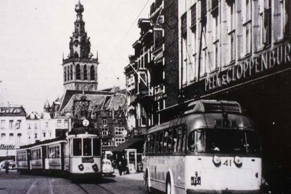 Oud en nieuw ontmoeten elkaar in de Korte Burchtstraat. Een situatie die tussen 1952 en 1955 mogelijk was. Trolley 41 op lijn 1 aan de halte bij Peek & Cloppenburg. Terwijl motorwagen 26 de voor de dienst op lijn 2 benodigde aanhangrijtuigen van de remise naar Kelfkensbos brengt.