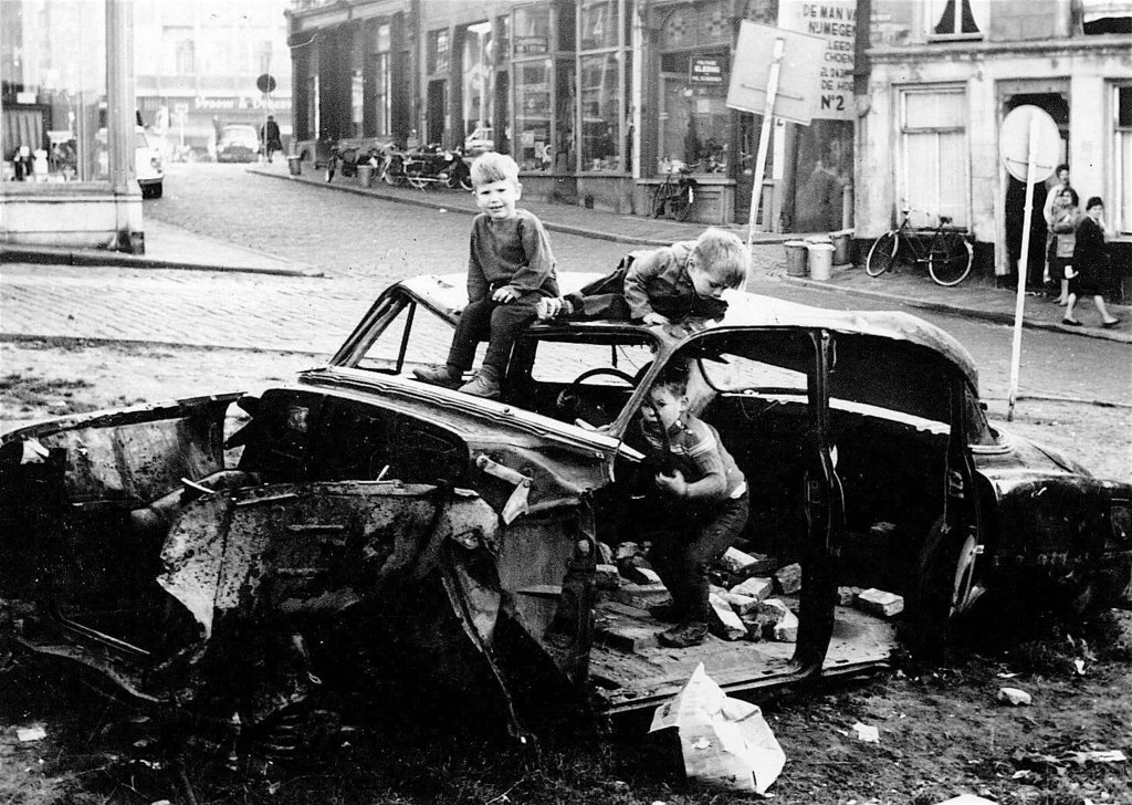 Spelende kinderen in een autowrak halverwege de jaren '60 van de vorige eeuw. De foto is genomen op de hoek van de Korenmarkt en de Kannenmarkt. Links op de achtergrond nog net zichtbaar de belettering van Vroom & Dreesman op de Grote Markt.
