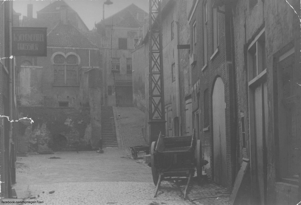 Vanaf de Lage Markt kijken we in de richting van de Nonnenstraat, de trap op. Links daarvan zien we de achterzijde van de Joodse Synagoge. Aan het begin van de veertiende eeuw was Nijmegen de belangrijkste Joodse vestiging van het land. De gemeenschap werd verwoest bij de pestepidemie van 1349. Hierna vestigden zich wederom Joden in de stad en een eerste synagoge wordt aan het begin van de vijftiende eeuw vermeld als Schola Judeorum in de huidige benedenstad aan het Jodengasch. De Joodse gemeenschap in Nijmegen verdween weer aan het einde van die eeuw. In de zeventiende eeuw is er weer een Joodse gemeenschap in de stad en er was een huissynagoge aan de Vleeschhouwersstraat die in 1697 na klachten gesloten werd door de gemeente. Hierna werd een voormalige herberg aan de Groote Straat als gebedsruimte gebruikt. Op 5 september 1756 werd de synagoge aan de Nonnenstraat in gebruik genomen. De Joodse gemeenschap vestigde hierna in aangrenzende panden een Joodse school en bad. In 1804 werd Nijmegen het opperrabbinaat van Gelderland. In 1881 ging het opperrabbinaat naar Arnhem. In 1872 werd naast de synagoge een school gebouwd in quasi-oosterse stijl naar ontwerp van gemeentearchitect Pieter van der Kemp. De synagoge werd begin twintigste eeuw te klein en werd verkocht.