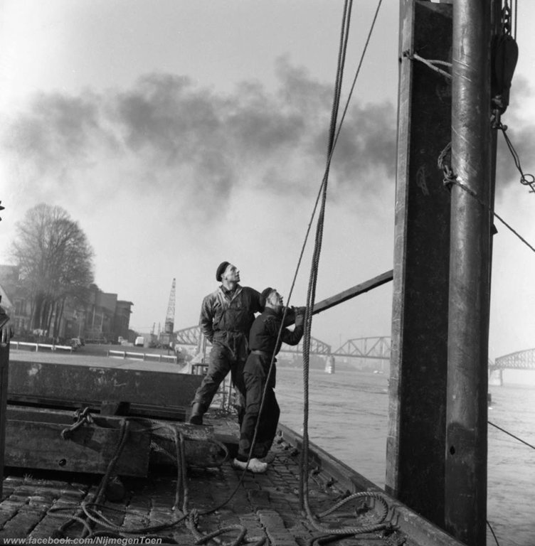 Ook in de jaren '50 van de vorige eeuw werd er hard gewerkt aan de Waalkade zoals we zien op deze mooie foto van de heer Polkamp. De mannen op de foto werken aan de damwand van de kade. Op de achtergrond zien we een kraan voor het laden en lossen van goederen vanuit de schepen en de spoorbrug. Een speciale dank gaat uit naar de erven van de familie Polkamp voor het beschikbaar stellen van deze unieke foto.