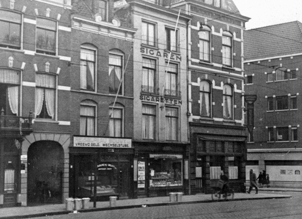 Kelfkensbos omstreeks 1939 met v.l.n.r. vanaf de poort reisbureau Bouvy, daarnaast tabakswinkel van Van Steensel (filiaal van de zaak op de Grote Markt) en op de hoek met de Hertogstraat café de Roemer met op de achtergrond rechts het winkel- en wooncomplex in aanbouw aan de Burchtstraat op de plaats van de in 1934 gesloopte schouwburg.