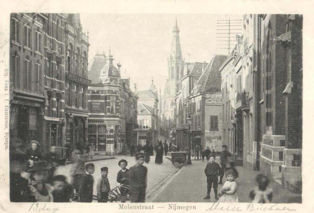 Een blik in de (Korte) Molenstraat, net voor het kruispunt met de Houtstraat, Broerstraat en de Pauwelstraat. Het is omstreeks 1899 wanneer een fotograaf ter hoogte van de St. Ignatiuskerk deze foto maakt onder belangstelling van de Nijmeegse jeugd.