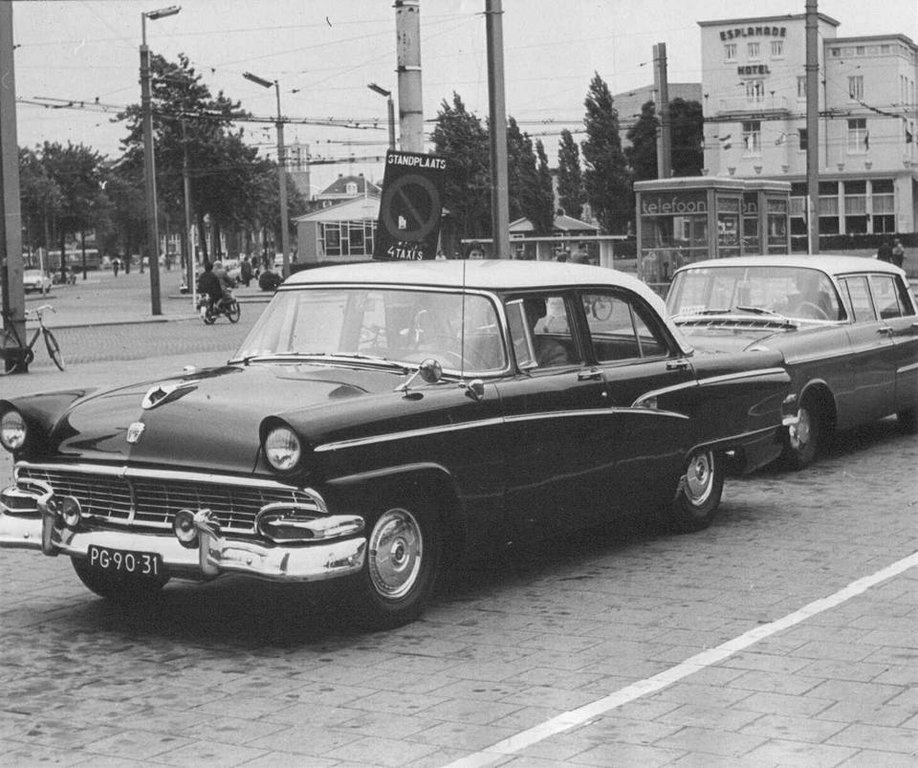 Een tweetal wachtende taxi's op de taxi standplaats aan het Stationsplein in 1962. Er is veel te zien op deze foto zoals rechts Hotel Esplanade op de Van Schaeck Mathonsingel. Het Hotel is inmiddels gesloopt na de brand van het toenmalige Chinees restaurant Fong Shou in 2008. De telefooncellen achter de taxi's waren in die tijd natuurlijk ook een bekend straatbeeld. Links op de foto zien we nog net de toren van de Molenstraatkerk en uiterst links de Spoorstraat waar nu de tunnel onder het station doorloopt. De tunnel werd geopend in 1966. Ook de bovenleidingen van de Trolleybus zijn duidelijk zichtbaar.