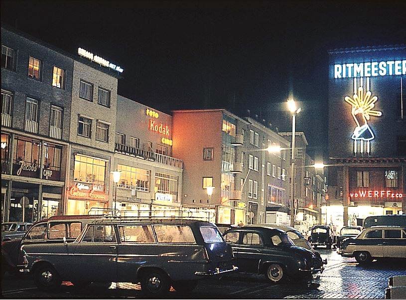 In de jaren '60 zag Plein 1944 er prachtig uit in het donker; mooi verlicht en met veel gebruik van neon. Vooral de grote Ritmeester reclame viel op. Het plein werd ook gebruikt als parkeerplaats. Op de achtergrond zien we van links naar rechts o.a. Modehuis Jacobs, cafetaria Centrum Expresse, A. Holland Schoenwinkel, Foto Verweij, Parfumerie Albers en uiterst recht woninginrichter Van der Werff. Wie kent het nog terug?