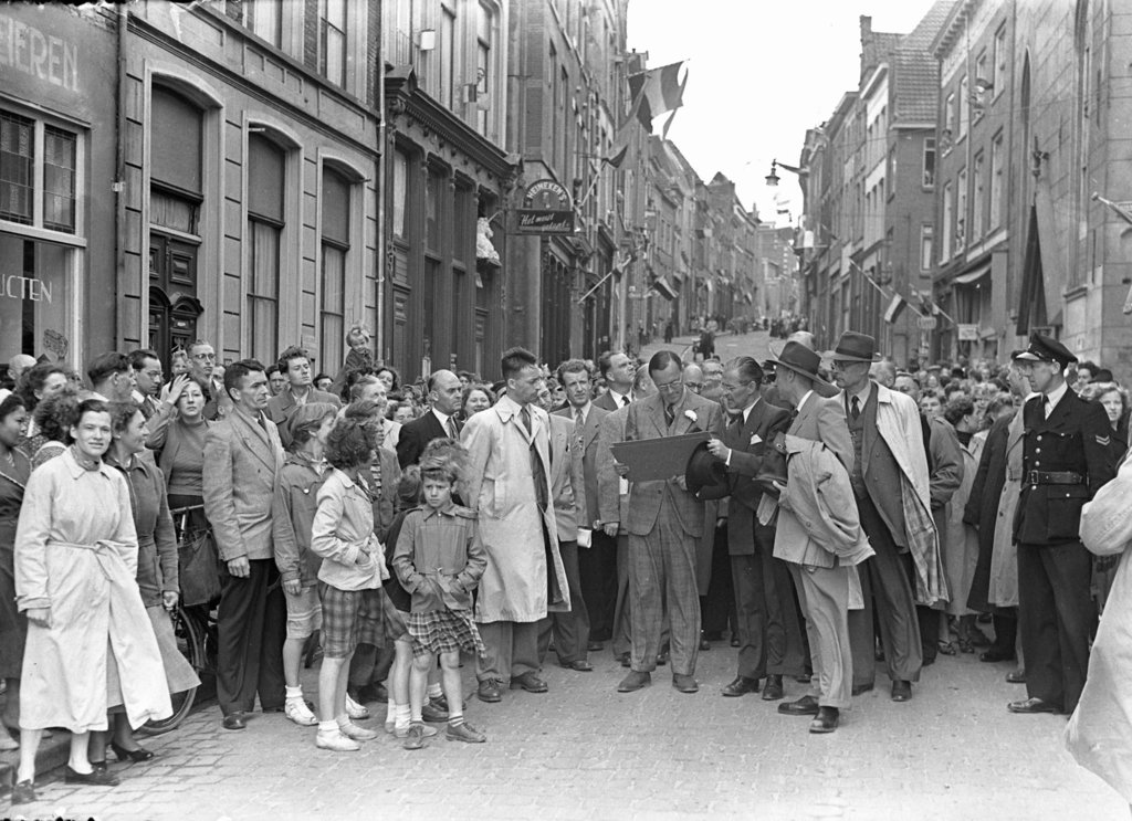 In 1953 bracht Prins Bernhard een bezoek aan Nijmegen. We zien de Prins hier tijdens een stadswandeling in de mooie Grotestraat in het gezelschap van o.a. burgemeester Hustinx (rechts) en veel belangstellenden. Overal in de straat hangen de vlaggen uit om de Prins te verwelkomen.
