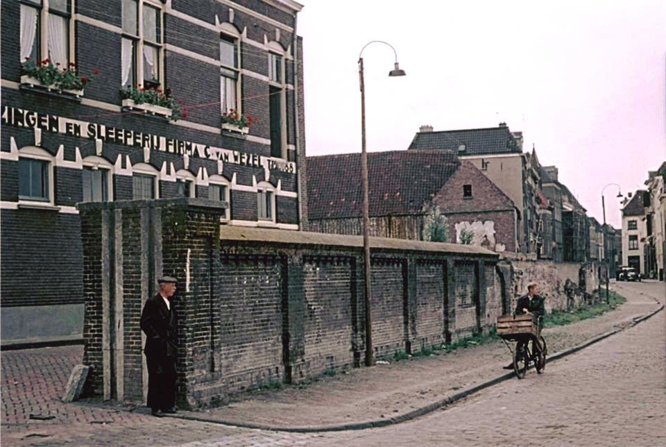 Een foto van Nijmegenaar Jeroen van Lith uit 1955. Op deze foto zien we de oude keermuur op de Waalkade ter hoogte van de Vosstraat met voorraan links de (af te sluiten) opening voor het doorgaande verkeer. De muur maakte deel uit van de hoogwaterkering, die - net zoals ook nu nog - de (beneden)stad bij hoog waterpeil van de Waal moest beschermen. Direct achter de muur de Achter de Vismarkt en het bedrijfspand van Verhuizingen en Sleeperij Firma C. van Wezel, nu volledig gesloopt. Op de achtergrond rechts, de Lage Markt.